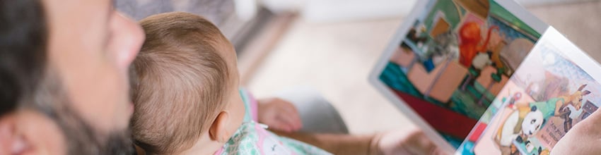 Isä lukee ääneen vauva sylissään, lahjaidea, joka vahvistaa läsnäoloa ja yhteistä aikaa vauvan ja tuoreen isän kanssa.