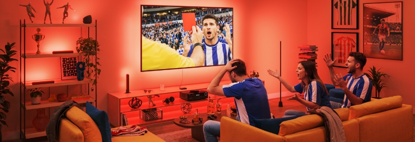 Ystävät juhlii jalkapallomaalin televisiossa voimakkaalla sinisellä WiZ Sports Live -valaistuksella olohuoneessa