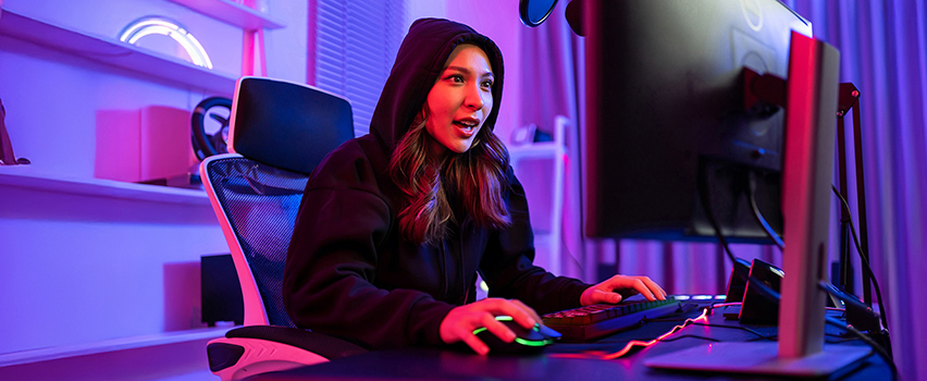 Nuori nainen pelaa tietokoneella Wozinsky gaming-hiirellä ja näppäimistöllä pimeässä huoneessa violetilla RGB-valaistuksella