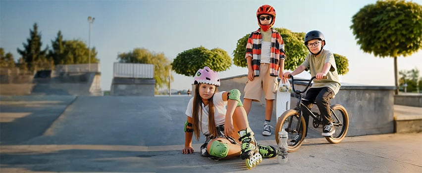 Kolme lasta Wozinsky kypärät ja suojavarusteet skateboard, rullaluistimet ja BMX-pyörä skeittiparkkissa